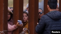 Migrantes se acercan desde la valla fronteriza para intentar cargar sus teléfonos en la frontera sur de EEUU. Foto: Reuters.