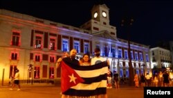 Manifestantes sostiene una bandera cubana mientras los colores de la bandera cubana se proyectan en la fachada de la sede del gobierno regional de Madrid en apoyo a las protestas antigubernamentales en Cuba, en Madrid, España, el 14 de julio de 2021. REUT