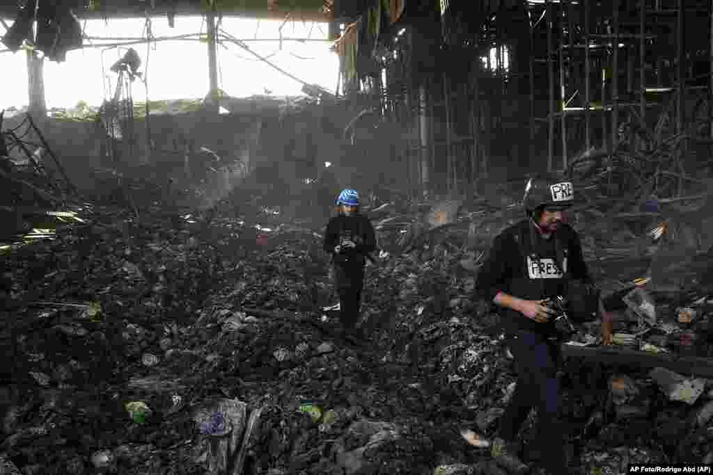 Unos periodistas caminan por el interior de un almacén de alimentos destruido, tras un ataque de Rusia hace doce días en Brovary, en las afueras de Kiev, Ucrania, el martes 29 de marzo de 2022. (AP Foto/Rodrigo Abd)