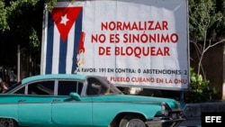 Un auto pasa junto a un cartel alusivo al embargo estadounidense a Cuba.