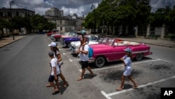 Turistas pasan frente a un estacionamiento lleno de autos clásicos estadounidenses que esperan a los clientes, en La Habana, en julio de 2022. (Foto AP/Ramón Espinosa)