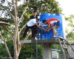 El técnico de “MedWater” Jeremias Neptali Tapuy Shiguango (de blanco) trabaja en un tanque de agua que suministra agua potable a una cocina comunitaria en Raya Yacu, provincia de Napo (Ecuador). (© MedWater)