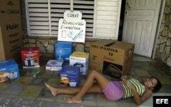 Una joven descansa en el portal de su casa que donde se muestran algunas cajas de los efectos electrodomésticos de la llamada "revolución energética" en Cuba.