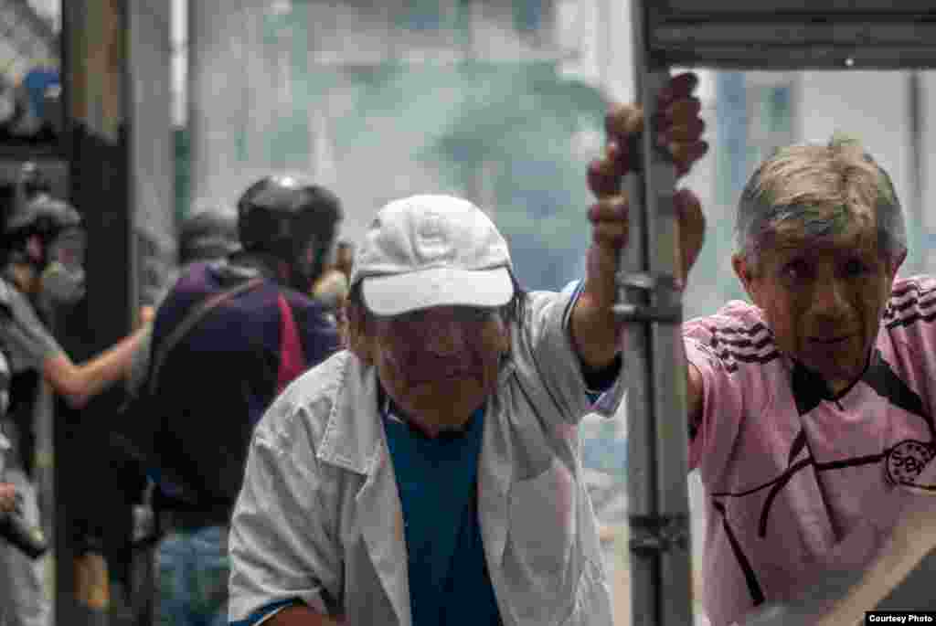 Comerciantes encargados de un puesto de comida rápida en Chacaito, quedan atrapados en el enfrentamiento y desplazan su carrito de comida en medio de gases lacrimógenos. (Foto: Juan Pablo Arraez)