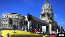 Dos turistas viajan en un viejo auto descapotable por una calle de La Habana. 