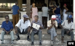 Un grupo de ancianos conversan sentados en un muro mientras esperan la llegada del periódico.