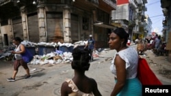 Personas caminan en La Habana entre montones de basura y comercios informales. 