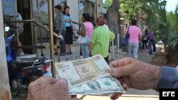 Un hombre muestra un peso convertible cubano y un dólar estadounidense frente a una oficina de la Western Union en La Habana.