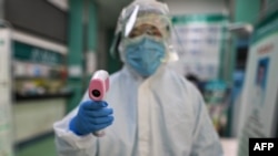 Una técnica de salud se dispone a tomarle la temperatura en Wuhan a un fotógrafo de la agencia AFP (Héctor Retamal/AFP).